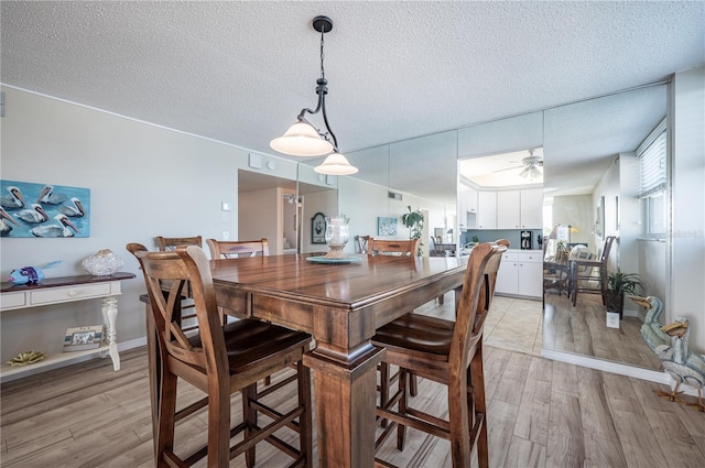 dining room with ceiling fan, a textured ceiling, and light wood-type flooring