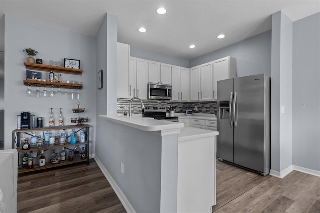 kitchen featuring wood-type flooring, kitchen peninsula, white cabinets, stainless steel appliances, and backsplash