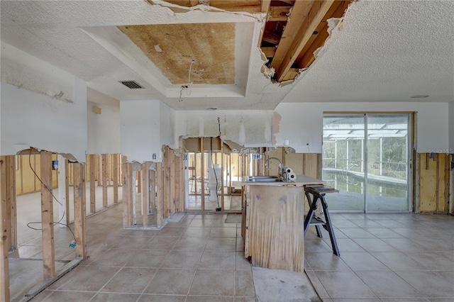 kitchen with light tile patterned flooring, a tray ceiling, sink, and a textured ceiling