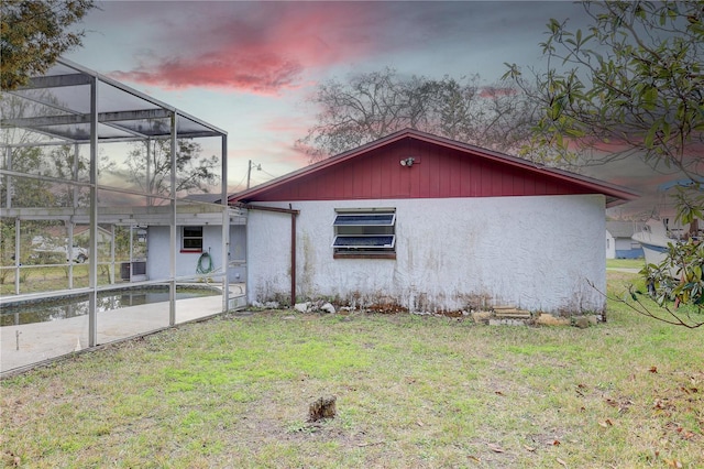 back house at dusk featuring a lanai and a lawn