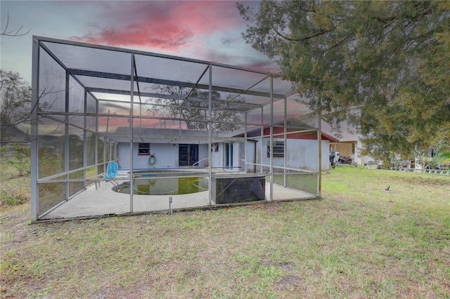 back house at dusk featuring a patio, a lanai, and a lawn