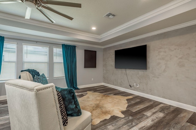 living room featuring dark wood-type flooring, ceiling fan, ornamental molding, and a raised ceiling