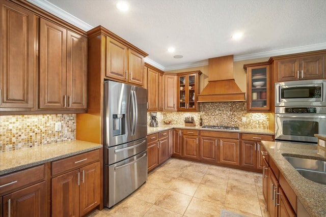 kitchen with premium range hood, backsplash, stainless steel appliances, crown molding, and light stone countertops