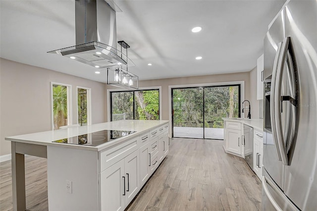 kitchen with appliances with stainless steel finishes, a kitchen island with sink, hanging light fixtures, white cabinets, and island exhaust hood