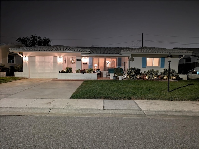 single story home with a tile roof, a lawn, stucco siding, a garage, and driveway