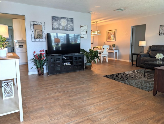 living area with baseboards, visible vents, light wood-type flooring, and a textured ceiling