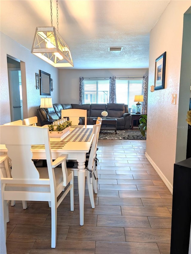 dining room featuring visible vents, a textured ceiling, wood tiled floor, and a textured wall