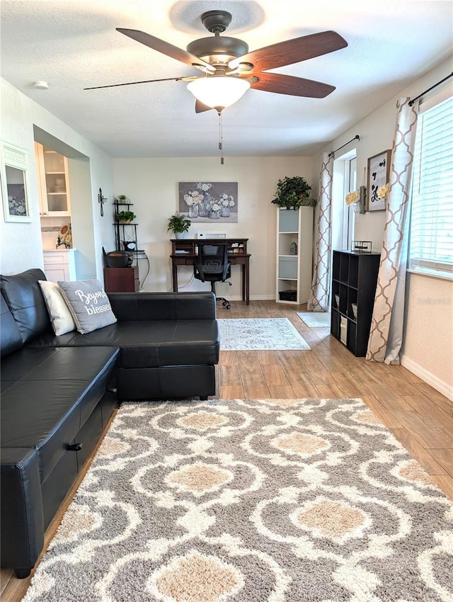 living area featuring built in shelves, baseboards, ceiling fan, wood finished floors, and a textured ceiling