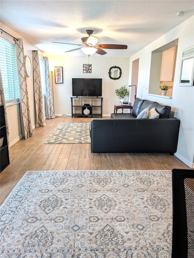 living room with baseboards, wood tiled floor, a ceiling fan, and a textured ceiling