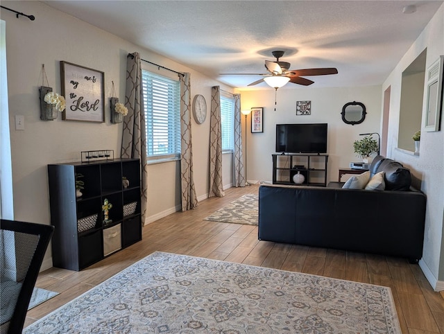 living area featuring a textured ceiling, baseboards, a ceiling fan, and wood finished floors