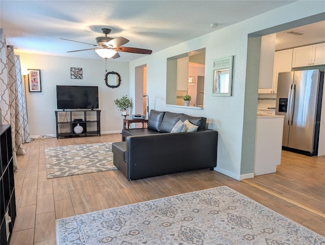 living room featuring visible vents, light wood-style flooring, a ceiling fan, and baseboards