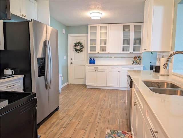 kitchen with a sink, white cabinets, glass insert cabinets, light wood-style floors, and a textured ceiling