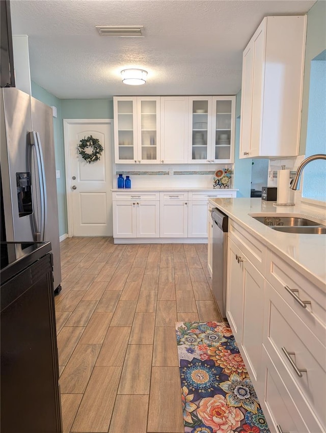 kitchen featuring wood tiled floor, light countertops, stainless steel appliances, white cabinetry, and a sink