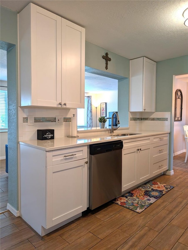 kitchen featuring stainless steel dishwasher, wood finish floors, white cabinetry, and a sink