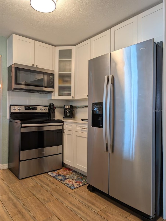 kitchen featuring wood finish floors, white cabinets, glass insert cabinets, appliances with stainless steel finishes, and a textured ceiling