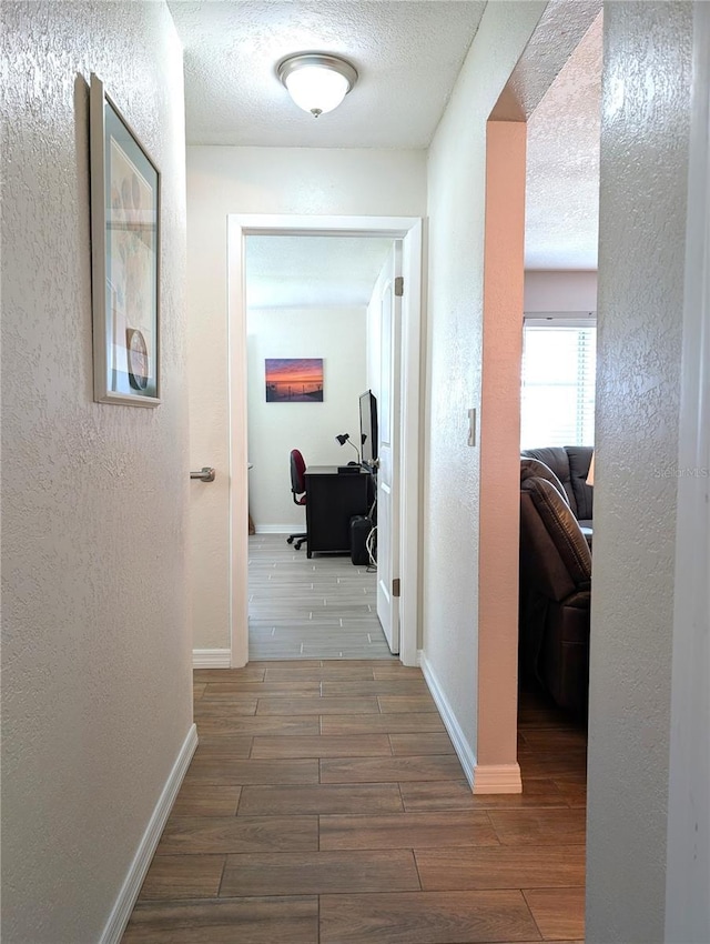 hall featuring baseboards, a textured ceiling, wood finish floors, and a textured wall