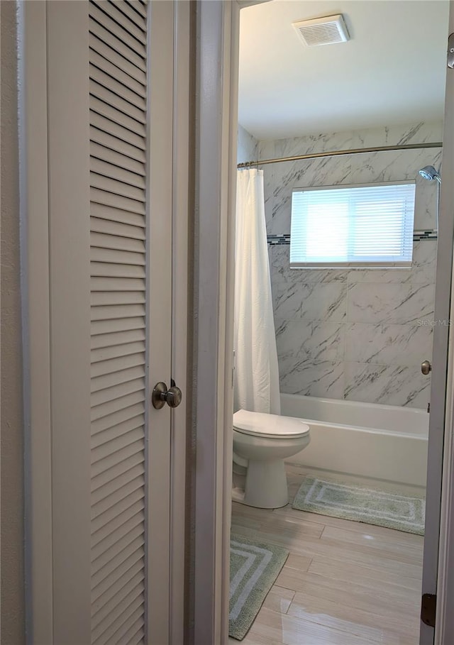 full bath with visible vents, toilet, shower / tub combo, wood finished floors, and a closet