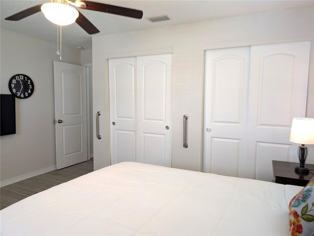 bedroom featuring visible vents, two closets, wood finished floors, baseboards, and ceiling fan