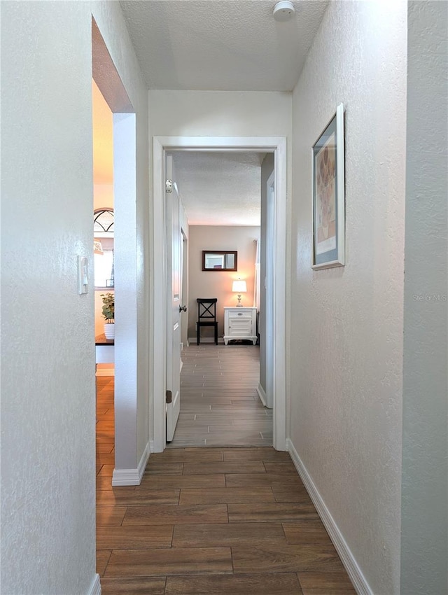 hallway featuring wood finish floors, baseboards, a textured ceiling, and a textured wall