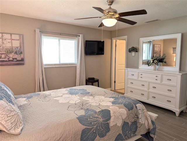 bedroom with dark wood finished floors, a ceiling fan, visible vents, and a textured ceiling