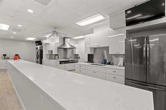 kitchen with white cabinets, freestanding refrigerator, wall chimney range hood, and a sink