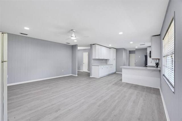 unfurnished living room with sink, ceiling fan, and light wood-type flooring