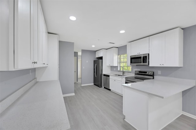 kitchen with light hardwood / wood-style flooring, stainless steel appliances, white cabinets, sink, and kitchen peninsula