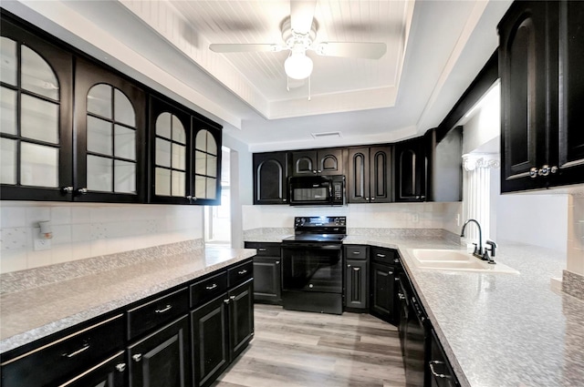 kitchen with sink, ceiling fan, black appliances, a raised ceiling, and light wood-type flooring