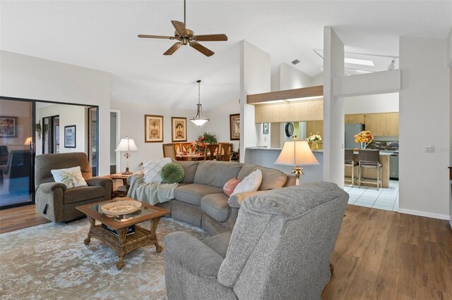 living room with ceiling fan, high vaulted ceiling, and light hardwood / wood-style flooring