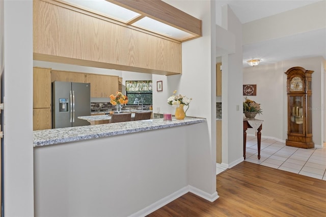 kitchen featuring stainless steel refrigerator with ice dispenser, light stone counters, a skylight, kitchen peninsula, and light hardwood / wood-style floors