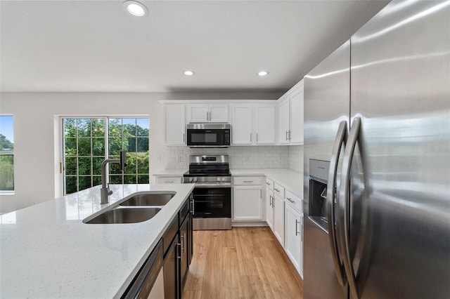 kitchen featuring sink, appliances with stainless steel finishes, backsplash, light stone countertops, and white cabinets