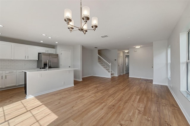 kitchen with light hardwood / wood-style flooring, stainless steel fridge, hanging light fixtures, and white cabinets