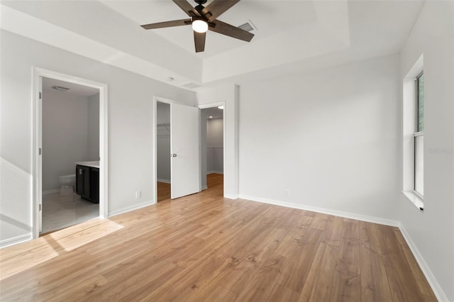 unfurnished bedroom featuring multiple windows, a spacious closet, light hardwood / wood-style floors, and a tray ceiling