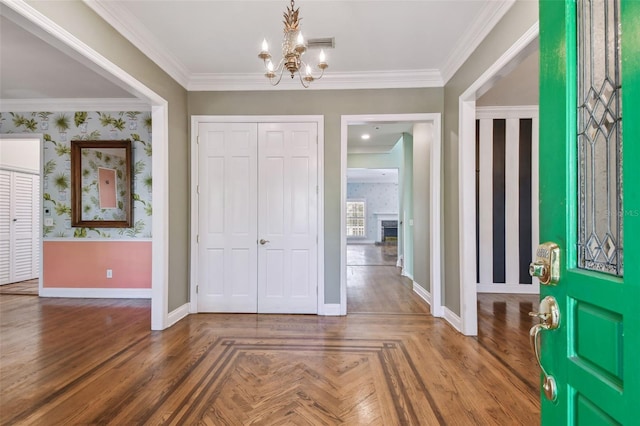 foyer entrance with a chandelier, ornamental molding, baseboards, and wallpapered walls