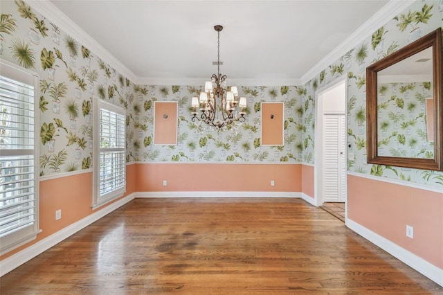 unfurnished dining area with a wainscoted wall, wood finished floors, a chandelier, baseboards, and wallpapered walls