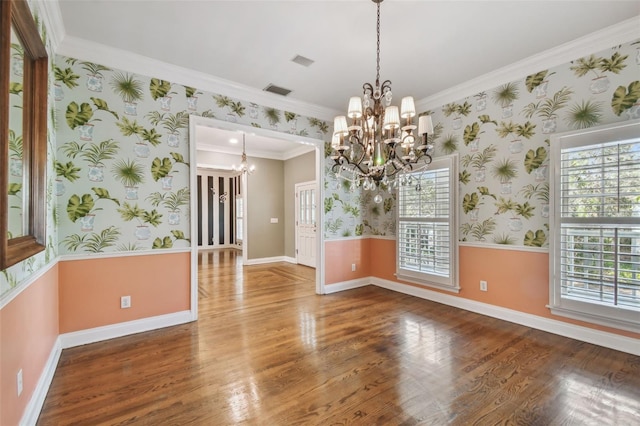 unfurnished dining area with wallpapered walls, a wealth of natural light, wood finished floors, and an inviting chandelier