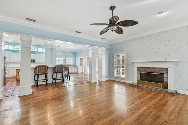 living room featuring ornamental molding, decorative columns, and wallpapered walls