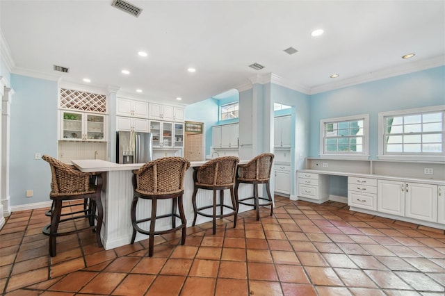 kitchen with built in desk, a breakfast bar area, stainless steel fridge, and visible vents