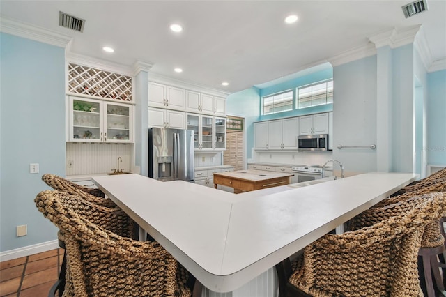 kitchen with visible vents, appliances with stainless steel finishes, a kitchen breakfast bar, and crown molding