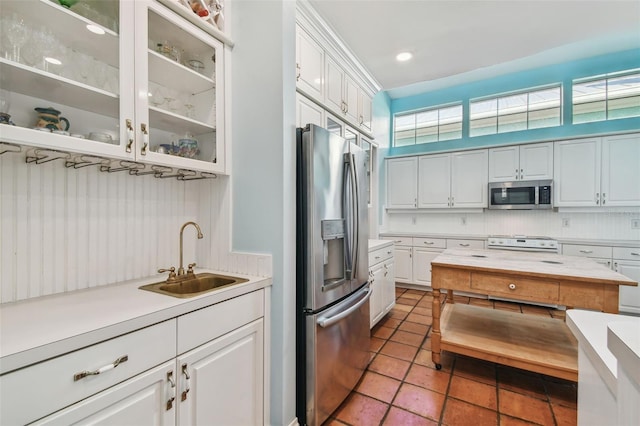 kitchen with stainless steel appliances, a sink, white cabinetry, light countertops, and glass insert cabinets