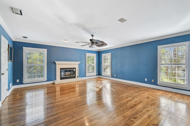 unfurnished living room featuring crown molding, visible vents, a glass covered fireplace, wood finished floors, and baseboards