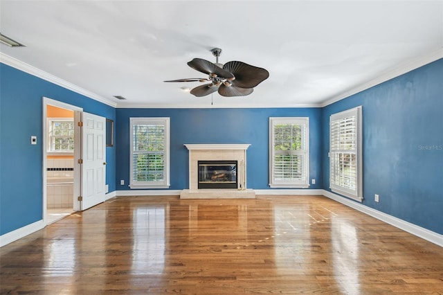 unfurnished living room with ornamental molding, wood finished floors, a glass covered fireplace, and a healthy amount of sunlight