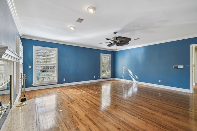 spare room featuring a glass covered fireplace, a healthy amount of sunlight, crown molding, and hardwood / wood-style floors