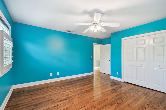 unfurnished bedroom with wood finished floors, a ceiling fan, visible vents, baseboards, and a closet