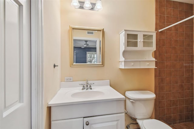 bathroom featuring toilet, visible vents, tiled shower, and vanity