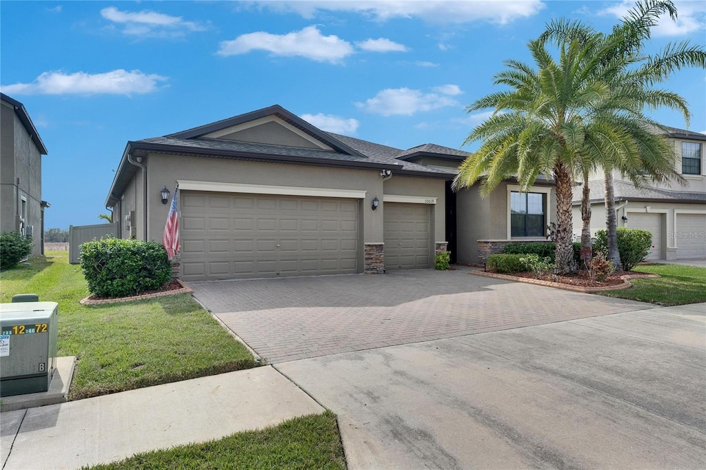 view of front of property with an attached garage, stucco siding, a front lawn, stone siding, and decorative driveway