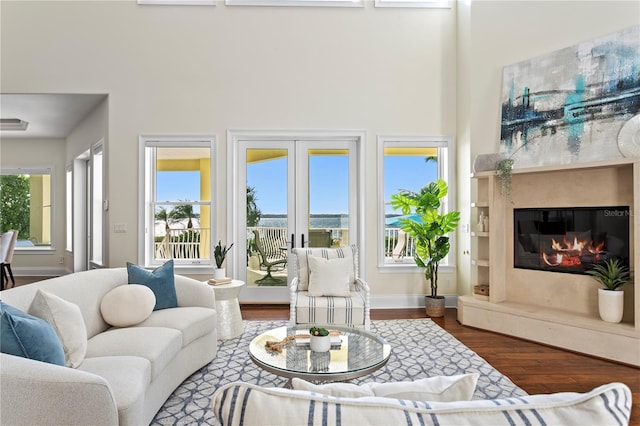 living area with wood finished floors, baseboards, a high ceiling, a fireplace, and french doors