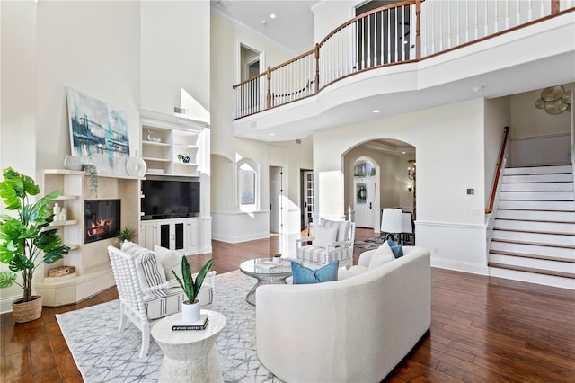 living area with crown molding, stairway, arched walkways, and wood-type flooring