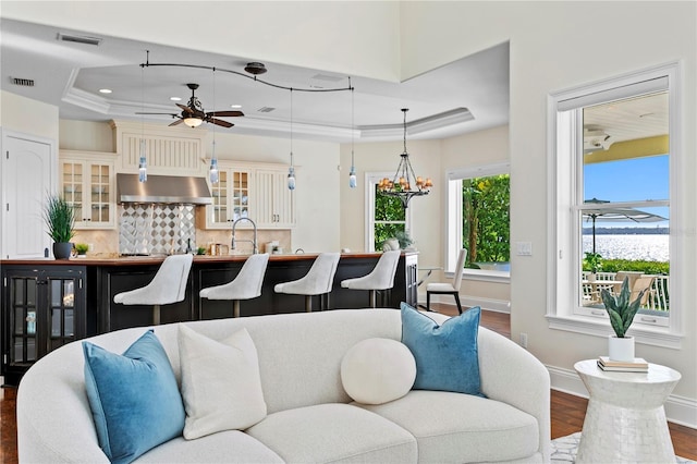 living room with dark wood-style floors, visible vents, a raised ceiling, and baseboards