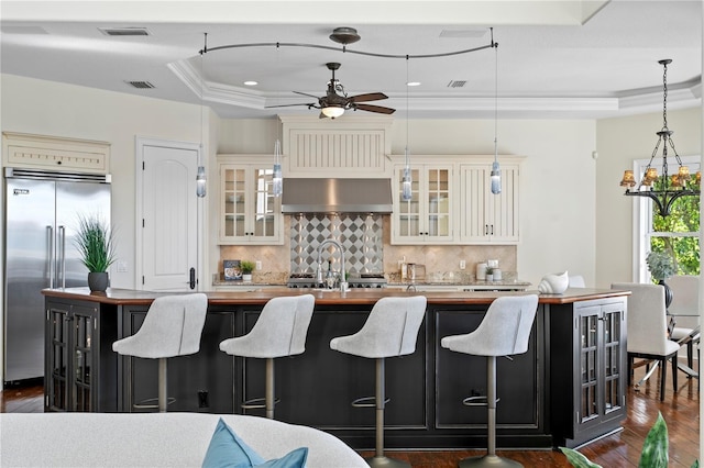 kitchen featuring visible vents, wooden counters, a tray ceiling, stainless steel built in fridge, and ceiling fan with notable chandelier